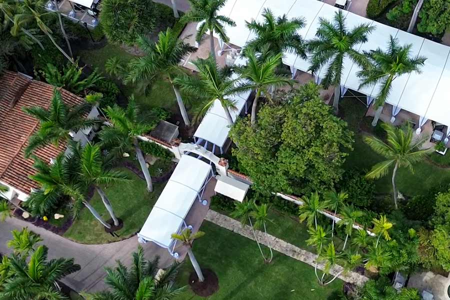 Aerial view of connected white walkway tents surrounded by palm trees at luxury venue.