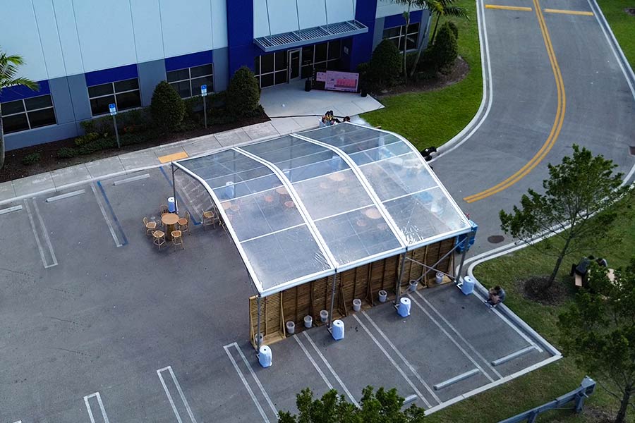 Clear arched tent with wooden walls and seating set up in a corporate parking lot.