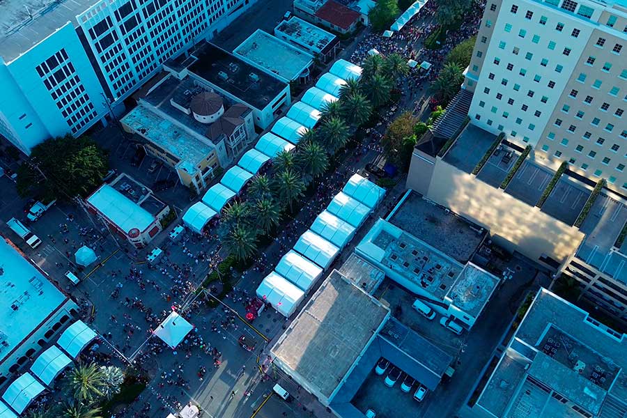 Aerial view of multiple connected party tents lining a city street festival surrounded by tall buildings.