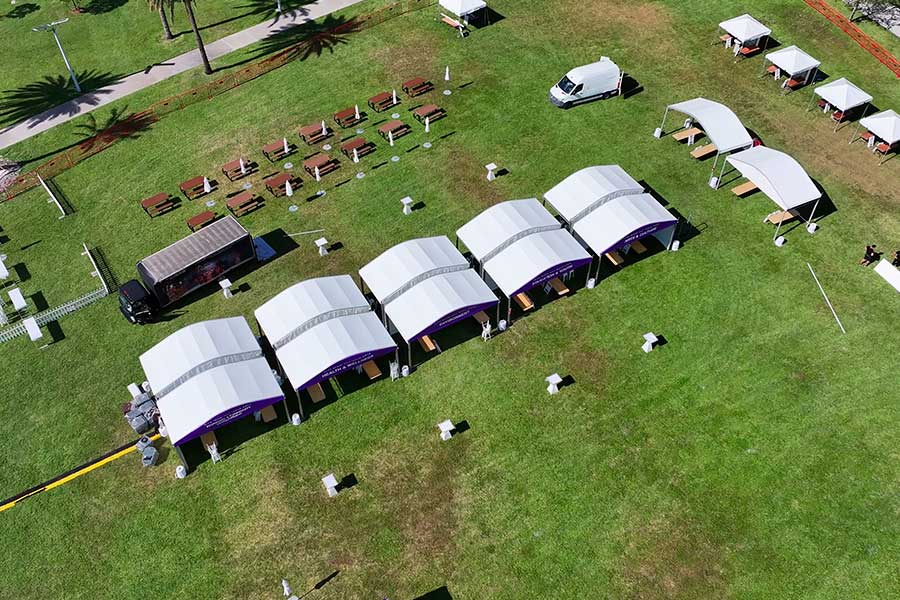 Aerial view of multiple white curved tents set up in a row on a large green lawn for an outdoor festival.