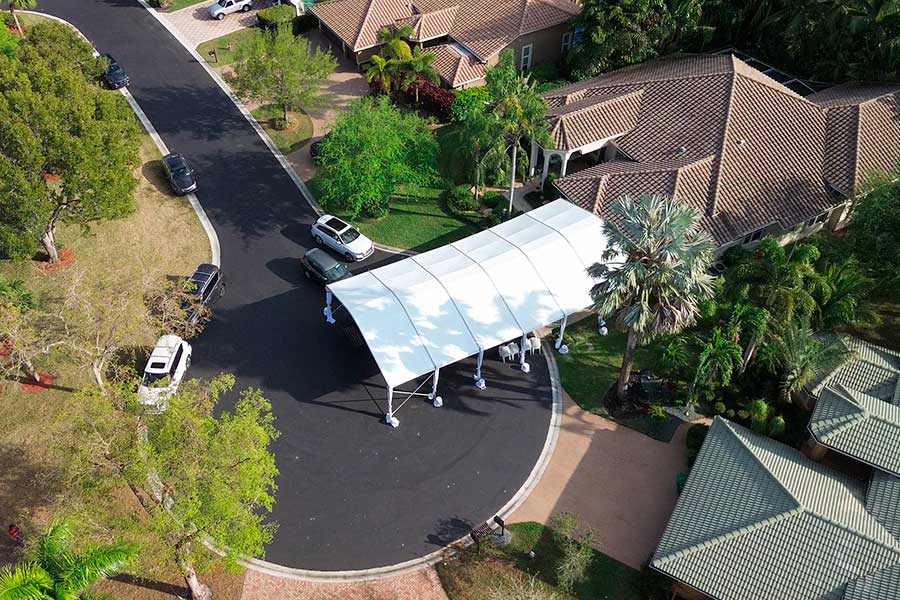 White frame tent set up over a curved residential driveway, perfect for a car cover or small gathering.