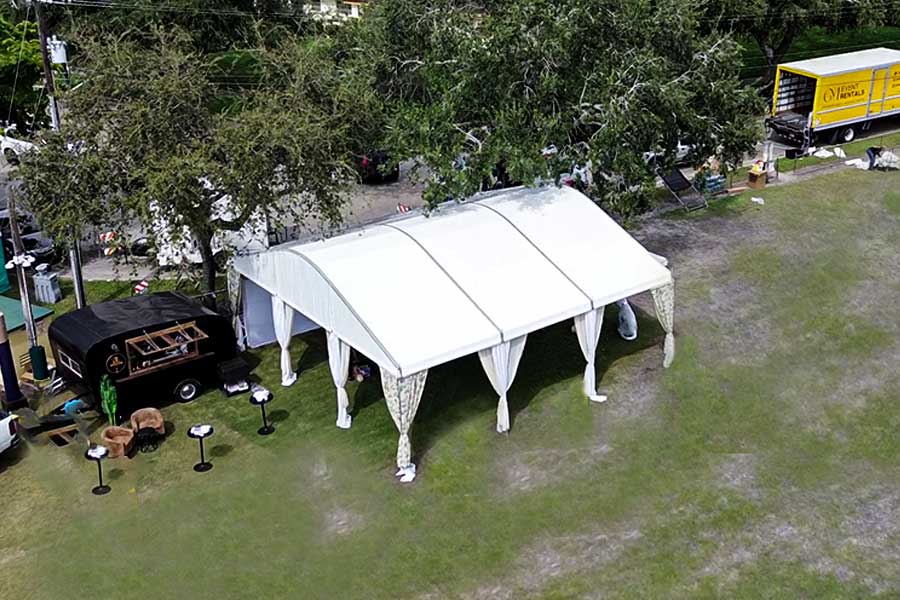 Large curved event tent and two peaked tents set up beside a commercial plant nursery.