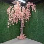 Artificial cherry blossom tree with cascading light pink blooms on a trunk base, statement floral décor for weddings and event photo backdrops.