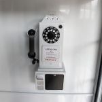White luxury telephone booth with glass panel doors and red interior flooring, photo booth-style wedding rental.