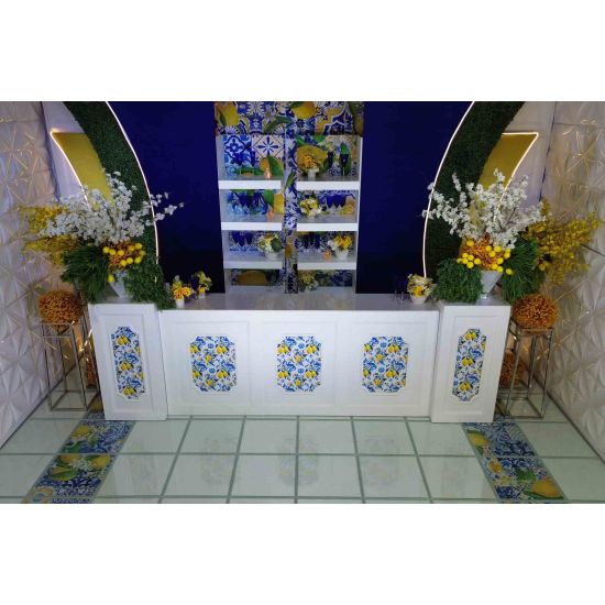 White bar set with blue-and-yellow lemon tile panels, matching back bar shelves, and lush white/yellow florals on a deep blue background.