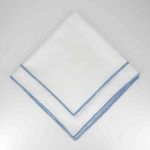 White Monarch napkin with blue border trim detail, folded in a triangle on a white plate for coastal weddings and elegant event settings