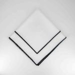 White Monarch napkin with black border trim detail, folded in a triangle on a white plate for modern formal weddings and event décor