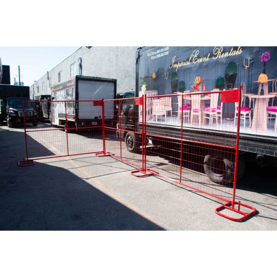 Red metal portable fence panel with wire mesh grid and stabilizing feet, temporary safety barrier for event perimeters, crowd control, and restricted areas