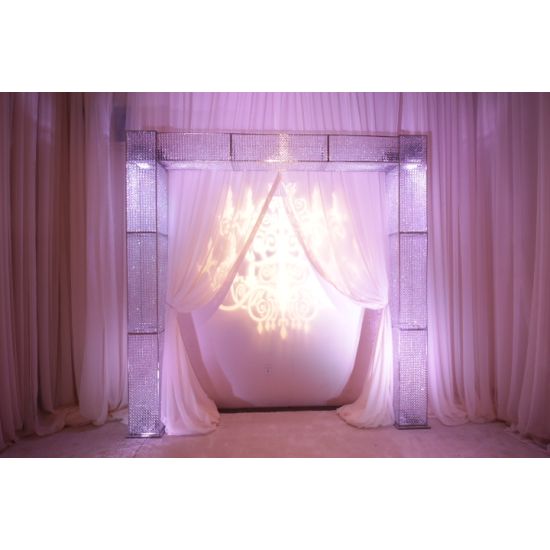 Single crystal entrance backdrop with soft draped fabric and chandelier glow, elegant event entryway feature for weddings and luxury décor.