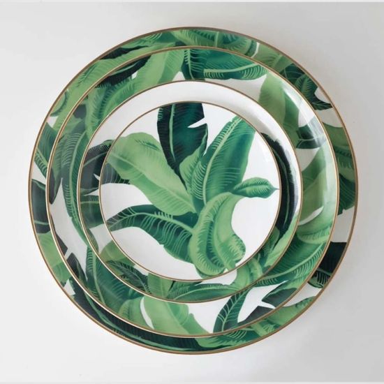 Banana leaf dinner plate with bold green foliage print framing the rim and gold edge, round design on a white background for tropical events