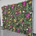 Green foliage wall backdrop with bright mixed flowers and tropical accents, colorful photo backdrop panel for parties and event décor.