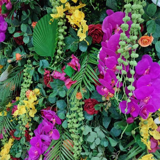 Green foliage wall backdrop with bright mixed flowers and tropical accents, colorful photo backdrop panel for parties and event décor.