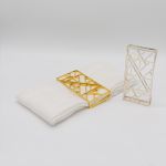 Geometric napkin holder with gold metal open-frame cube design holding a folded white cloth napkin, modern accent for event table settings