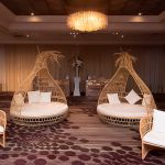 Bohemian wicker bed with teardrop canopy frame and cream cushion, statement lounge bed rental for boho weddings and outdoor events.