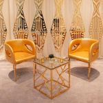 Gold trident accent armchair with smooth upholstery, curved back, gold-trim side cutouts, and sleek gold metal legs for luxury event lounge seating.